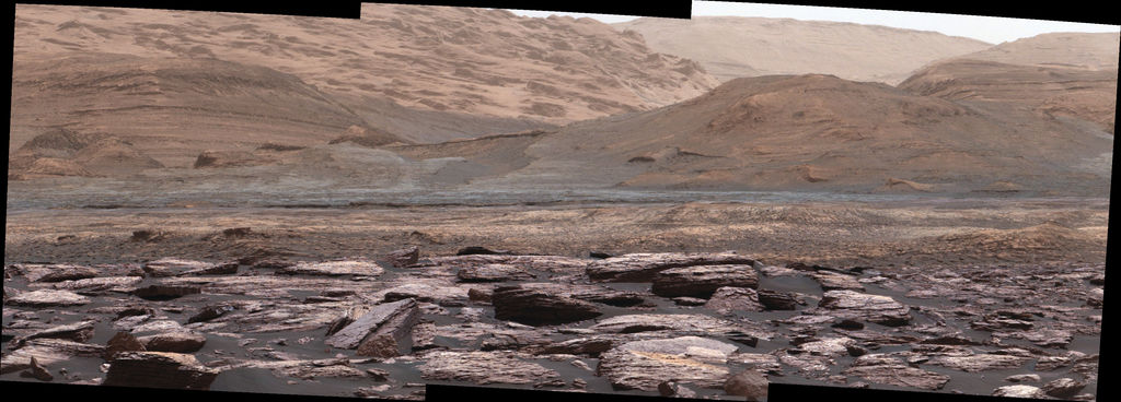 View of the path ahead for the Curiosity rover, looking toward the foothills of Mount Sharp. The various sedimentary layers on the mountain are a geological record of different environmental conditions in the past. Photo Credit: NASA/JPL-Caltech/MSSS